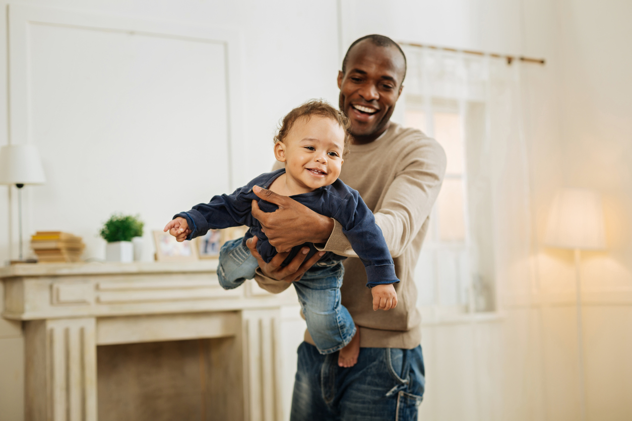 Cheerful, dark-haired man smiling and playing with his foster child while receiving monthly tax reimbursements